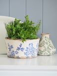 Hamptons-style blue and white floral ceramic planter pot with greenery, styled on a white shelf with coastal décor.
