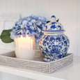 Blue and white ceramic ginger jar with lid styled on a rattan tray with candle and hydrangea flowers coastal home decor