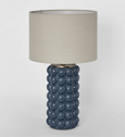 Blue ceramic table lamp with raised spherical base and linen shade on white background
