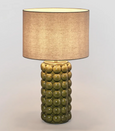 Green ceramic table lamp with raised spherical base and linen shade on white background