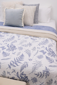 A reversible, quilted cotton coverlet with a blue and white botanical print of ferns and butterflies. One side is a white background with a blue print, and the reverse is a solid light blue with a white print.