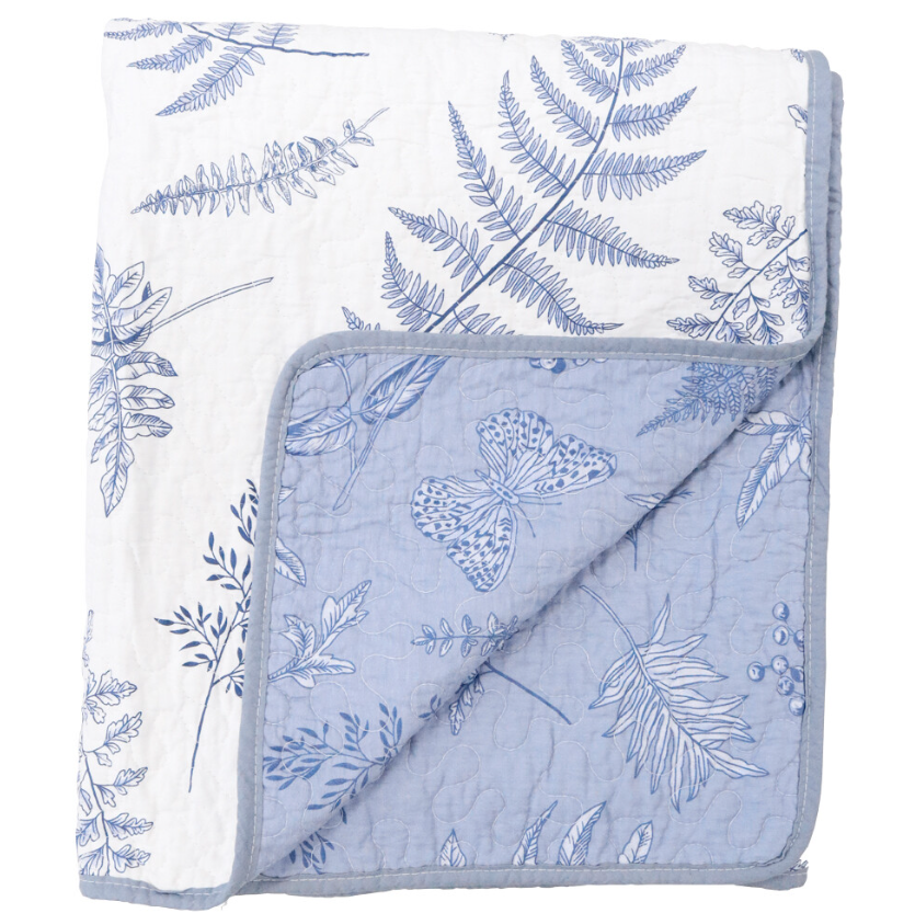 A reversible, quilted cotton coverlet with a blue and white botanical print of ferns and butterflies. One side is a white background with a blue print, and the reverse is a solid light blue with a white print.