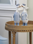 Duck captain and sailor figurines styled on a wooden side table in a coastal living space, wearing soft blue nautical uniforms.