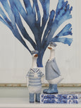 Duck captain and sailor figurines styled on a stack of books wearing soft blue nautical uniforms.