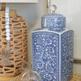 Blue and white floral canister styled on a woven tray beside a rattan table lamp in a Hamptons-inspired interior.