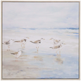 Framed coastal wall art featuring sandpipers walking along the shoreline, painted in soothing neutral tones with a light wooden frame.