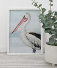 Framed coastal pelican print with white rattan frame, featuring detailed pelican illustration in blue and neutral tones.