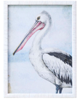 Framed coastal pelican print with white rattan frame, featuring detailed pelican illustration in blue and neutral tones.
