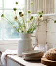 Large rustic white stoneware jug styled with flowers on a kitchen bench