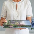 Person holding the Gardens of the Hamptons hardcover coffee table book showcasing its premium design and decorative spine detail