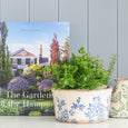 Gardens of the Hamptons coffee table book styled beside a blue botanical planter and greenery in a Hamptons-inspired interior setting