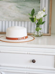 White and tan structured brim hat styled with vase and artwork