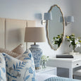 Medium dark natural linen drum lamp shade styled on a blue and white ceramic table lamp in a Hamptons coastal bedroom with white bedside table, botanical cushions and soft blue bedding.