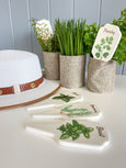 Ceramic herb garden stakes set with parsley, thyme and basil markers styled in linen pots beside a white sun hat in a Hamptons style interior.