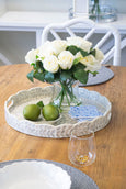 Decorative tray with flowers, limes, and a glass on a wooden table.