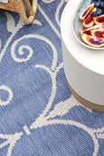 Blue and ivory flatweave outdoor rug featuring an elegant scroll pattern, styled in a Hamptons-inspired patio close up 