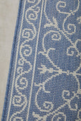 Blue and ivory flatweave outdoor rug featuring an elegant scroll pattern.