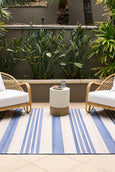 Blue and ivory striped flatweave outdoor rug styled in a coastal setting with rattan furniture, ideal for Hamptons or Malibu-inspired décor.