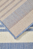 Blue and ivory striped flatweave outdoor rug styled in a coastal setting with rattan furniture, ideal for Hamptons or Malibu-inspired décor.