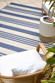 Blue and ivory striped flatweave outdoor rug styled in a coastal setting with rattan furniture, ideal for Hamptons or Malibu-inspired décor.