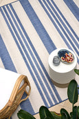 Blue and ivory striped flatweave outdoor rug styled in a coastal setting with rattan furniture, ideal for Hamptons or Malibu-inspired décor.
