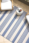 Blue and ivory striped flatweave outdoor rug styled in a coastal setting with rattan furniture, ideal for Hamptons or Malibu-inspired décor.