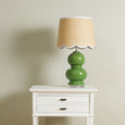 A tall, rectangular bedside table painted in a crisp white finish. It features two drawers stacked on top of an open lower shelf. The drawers have thin, streamlined black metallic handles, and the table legs are straight. Lamp sitting on top
