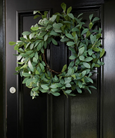 Large illuminated olive wreath with warm LED lights, hanging on a front door.