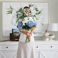 Woman holding a large blue and white hydrangea bouquet in a bright Hamptons-inspired interior with coastal decor.