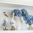 Coastal pelican figurines set of two in nautical blue and white resin styled on shelf with blue hydrangeas.