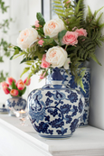 Blue and white ceramic posy jar with decorative lid, styled on a white mantel with soft pink roses, greenery and candlelight