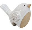 Small white ceramic pot sitter bird with sand-toned belly perched on the rim of a decorative pot filled with greenery.