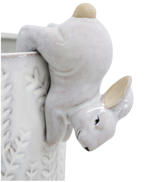 White ceramic rabbit pot sitter hanging upside down over the edge of a planter.