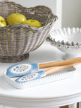 Blue floral kitchen spatula set with wooden handles resting on a white ceramic spoon rest, styled beside a woven fruit basket with green apples in a classic Hamptons-style kitchen.