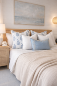 Coastal Hamptons style bedroom with blue and white patterned cushions, white piped cushions and soft ice blue velvet accent cushion on a timber bed