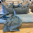 Ocean blue velvet throw draped across a bed with layered blue and neutral cushions creating a soft coastal bedroom styling look