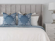 Rodeo silver velvet cushion styled on a bed with blue cushions and neutral bedding