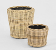 Set of two natural round rattan baskets with black inner pots for indoor plants.