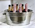 Polished stainless steel oval champagne bucket with dotted double-border design, filled with champagne bottles, perfect for entertaining.