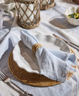 Seabrook pale blue linen napkin with softly frayed edges styled on a Hamptons-style table with rattan and ceramic accents