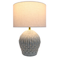Seabrook table lamp lit, showing warm glow through linen shade and textured ceramic base