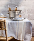 Pale blue and ecru striped linen tablecloth with softly frayed edges styled on a Hamptons-style dining table