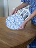 lady holding a blue and white floral pattern round trivet or placemat to show the beautiful pattern.