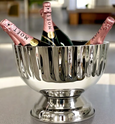 Polished stainless steel footed champagne bucket with fluted detailing, filled with champagne bottles — elegant design for stylish entertaining.