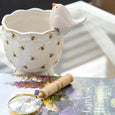 Apiary Ceramic Pot 15cm Soft Gold featuring delicate bee motifs and a scalloped rim, styled with a decorative bird accent atop a Hamptons garden book and brass magnifying glass.