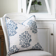 Bellamy Garden Cushion Coastal Blue 50cm styled on a white rattan chair, showing its blue botanical print and coordinating piped edge.