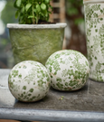 Green and white botanical decorative garden spheres styled with potted plants in an outdoor setting.