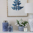 Blue and white motif canisters styled with white table lamp, floral arrangement and coastal artwork in a Hamptons-inspired interior.