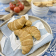 Chambray blue and white striped cotton napkin styled with croissants on a relaxed blue and white coastal breakfast table.