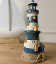 Navy and white Coastal Lighthouse Tealight Holder illuminated with a warm glow through the windows and doorway.
